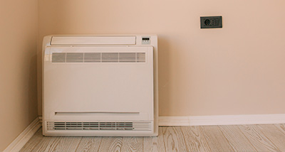 a floor mounted air conditioning system on a wooden floor against at beige wall